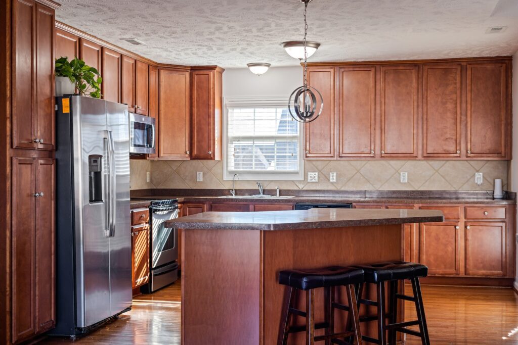 A Counter with Stools Near the Wooden Cabinets and Appliances at the Kitchen